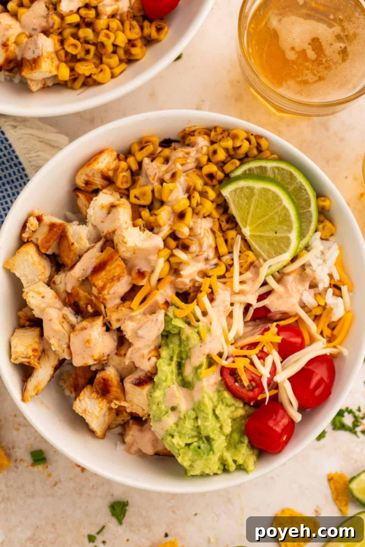 Close up of a taco bowl topped with diced chicken, charred corn, cherry tomatoes, guacamole and shredded cheese.
