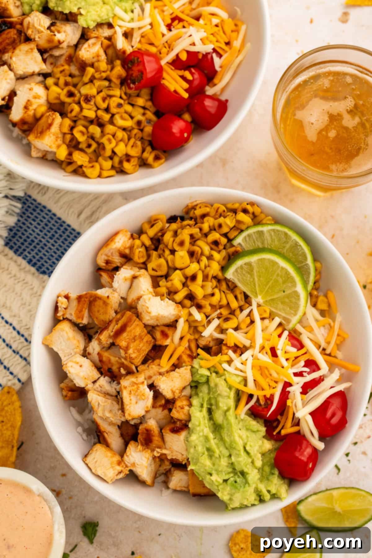 Rice bowls topped with chopped chicken, guacamole, cooked tomatoes, charred corn, shredded cheese and lime wedges.