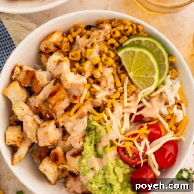 Close up of a taco bowl topped with diced chicken, charred corn, cherry tomatoes, guacamole and shredded cheese.