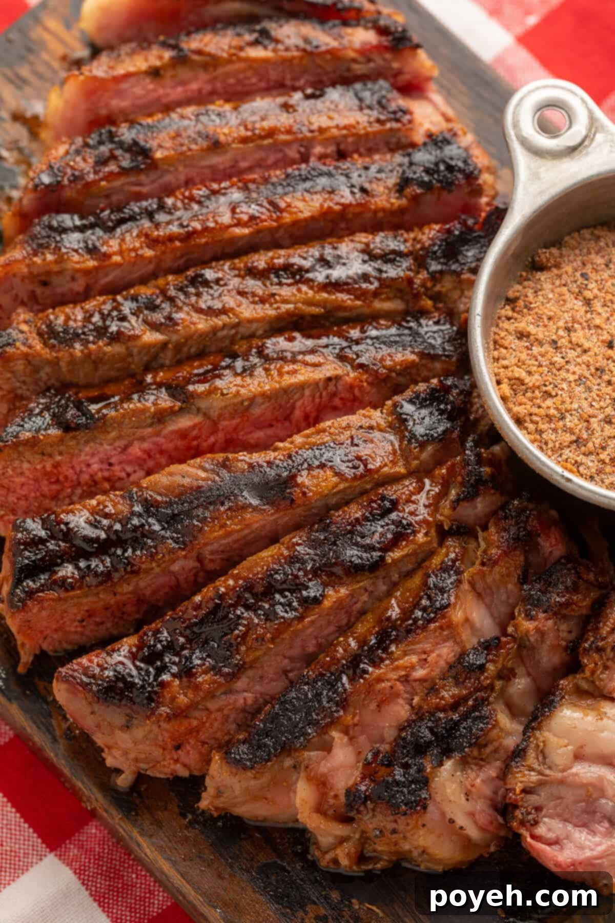 Close up of a sliced steak next to a metal measuring cup of steak seasoning.