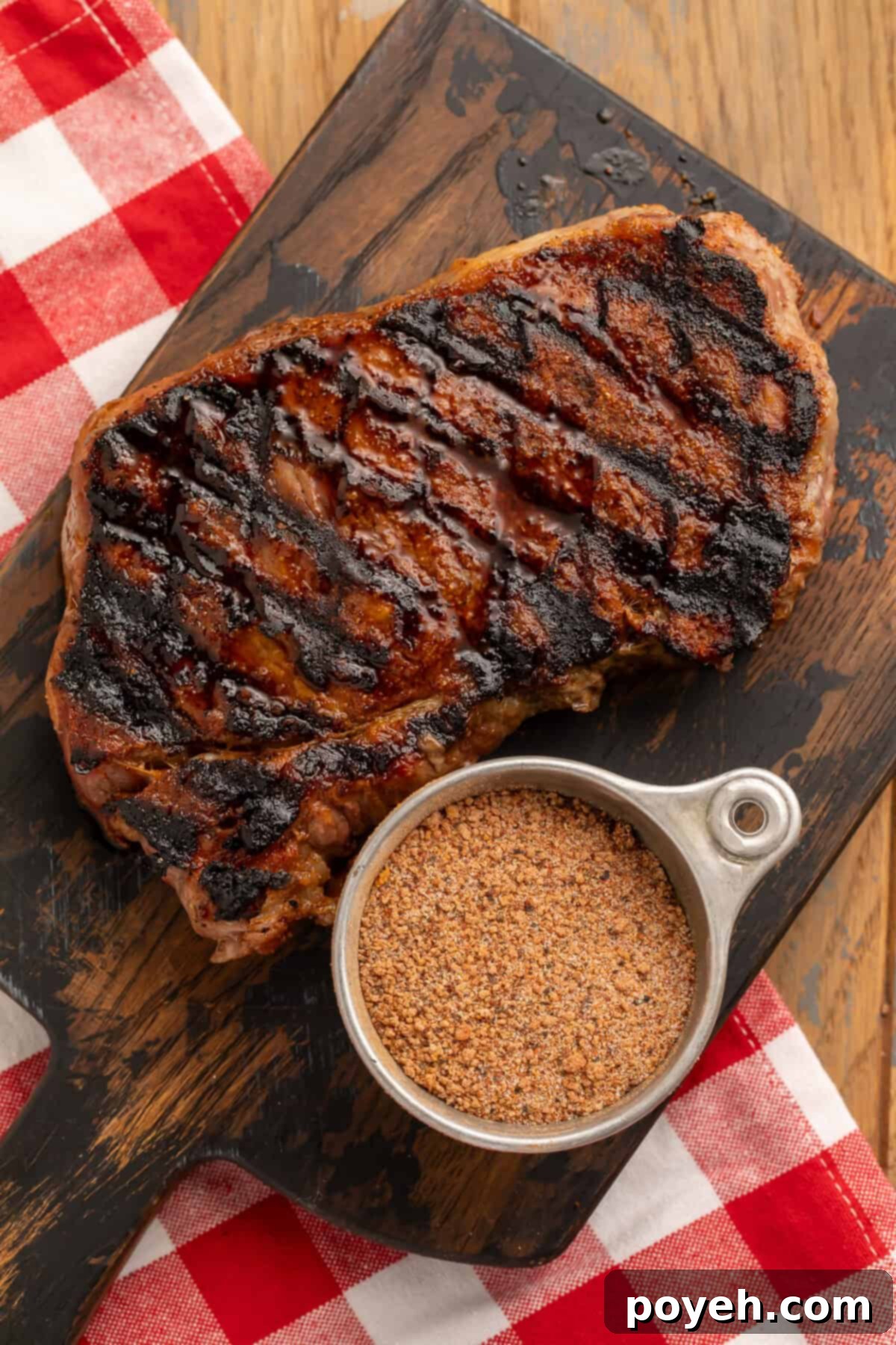 Grilled steak on a wooden board with a cup of steak seasoning.