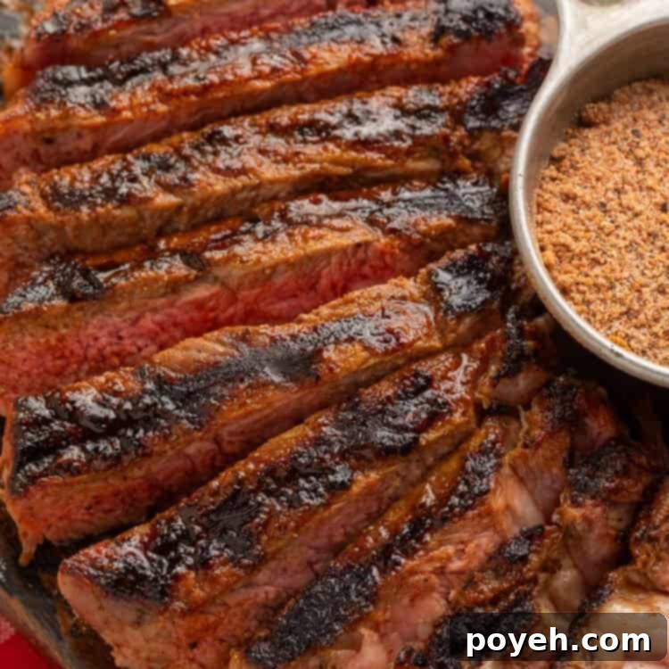 Close up of a sliced steak next to a metal measuring cup of steak seasoning.